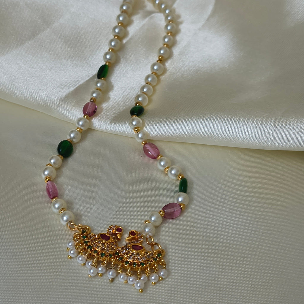 Pearl necklace with colored beads and gold clasp on a white fabric background
