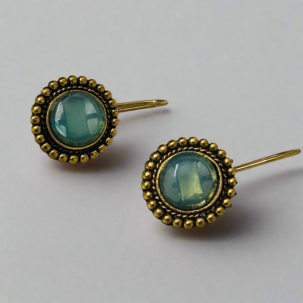 Pair of gold earrings with green gemstones on a white fabric background