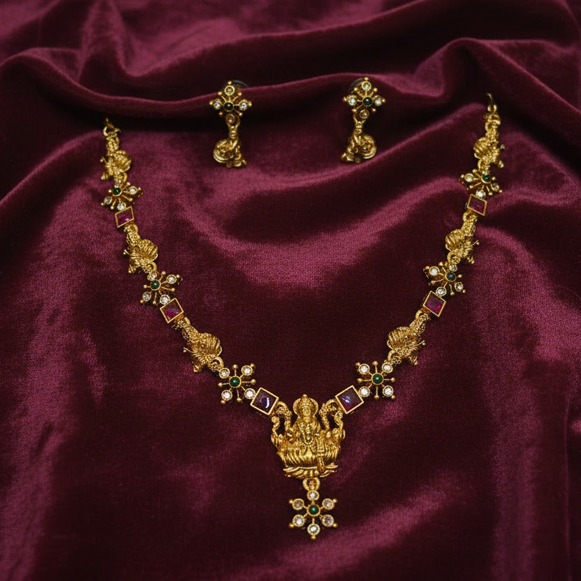Gold necklace with red stones on a black stand held by a hand against a plain background